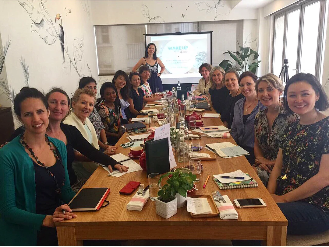 The full table at the Wake Up with Willo breakfast gathering in Hong Kong, Willo standing at the head of the table in front of the Wake Up with Willo slide